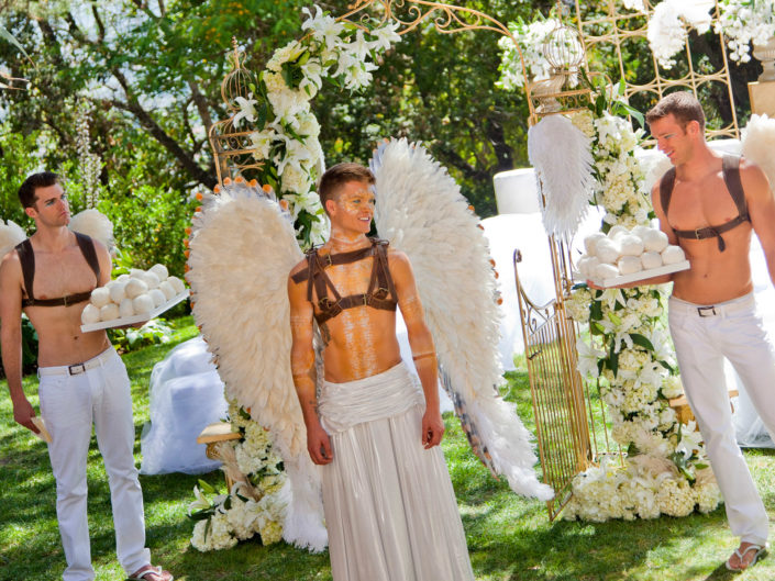 Heaven and hell wedding, heaven and hell themed wedding, shirtless men, winged men, angels with wings, angels, white wedding, wedding decor, wedding design, live angels, white fashion, ceremony, wedding reception, wedding servers, servers in costumes, white floral design, gay wedding, entrance to heaven, gay heaven, gold accents, men in makeup, leather straps, outdoor wedding, outdoor wedding reception, threesome