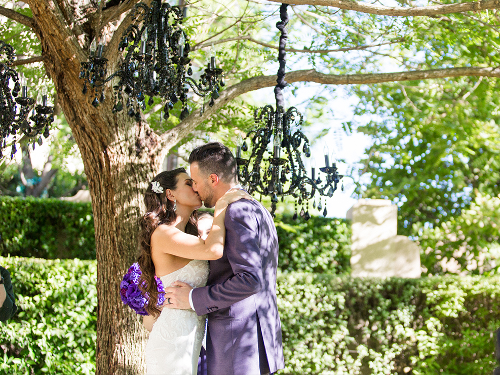 Bride and groom kissing under a chandelier tree, wedding photography, newlyewds, purple tuxedo, gothic wedding accents, produced by Kristin Banta Events